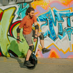 Rider performing tricks on INMOTION V5 unicycle near vibrant street art.