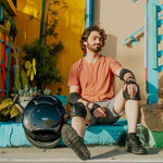 Man relaxing beside INMOTION V5 unicycle in a colorful urban environment